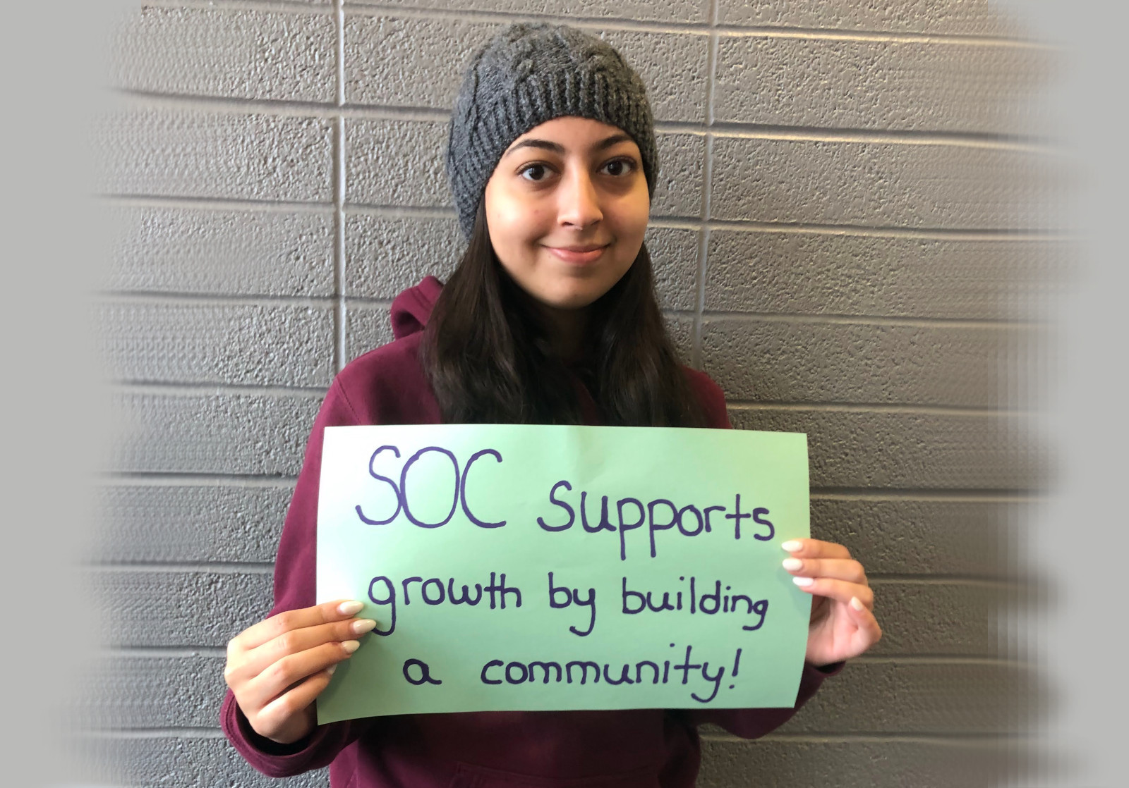 Student holding a sign that says "SOC supports growth by building a community Student holding a sign that says "SOC supports growth by building a community!"
